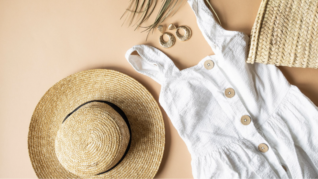A summer outfit lying on a tan backdrop. A summer dress and hot